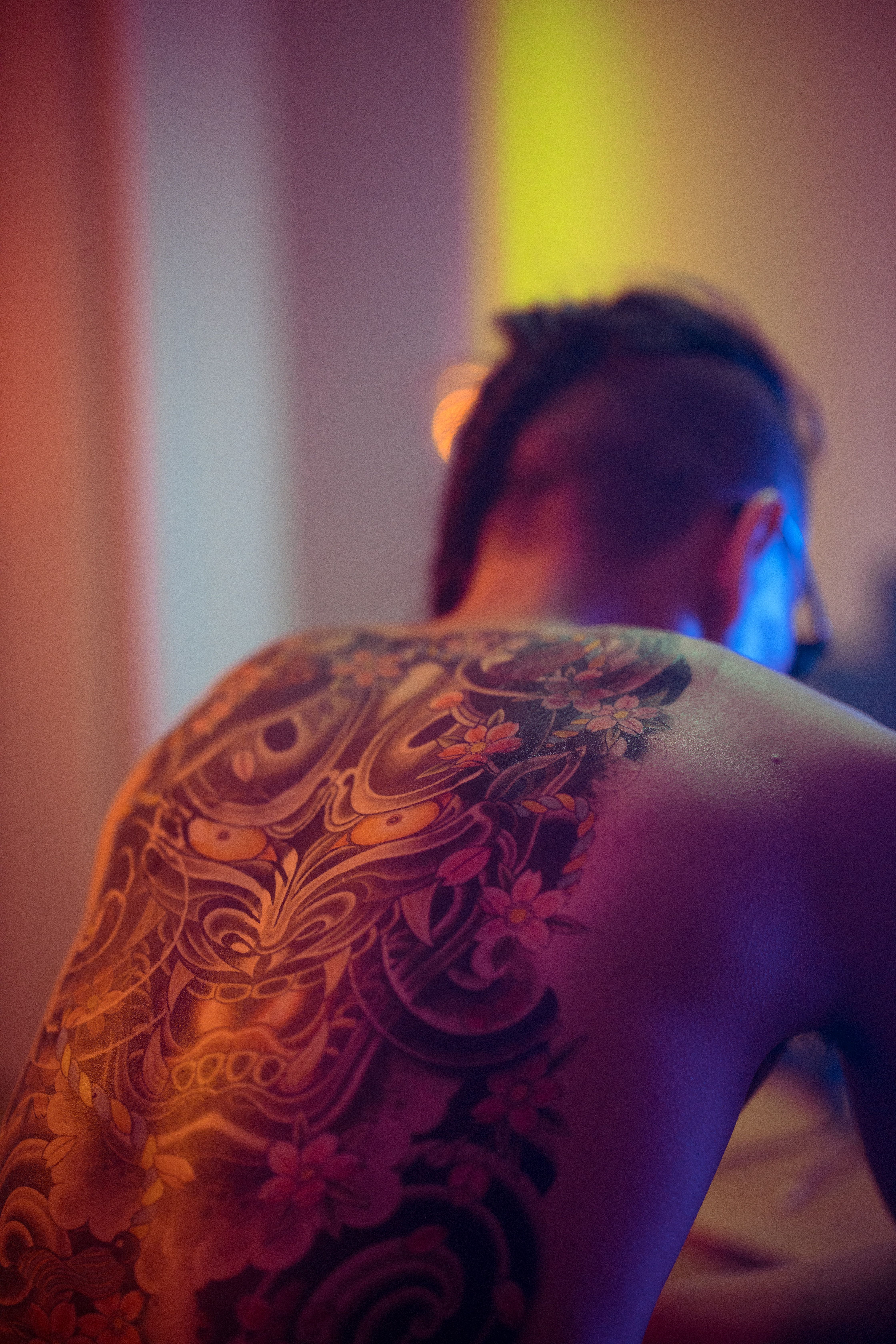 Homem de costas com irezumi de tronco inteiro em iluminação dramática